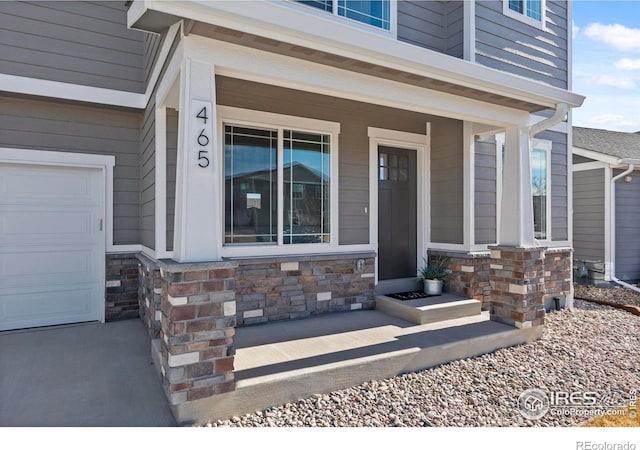 entrance to property with a garage, stone siding, and covered porch