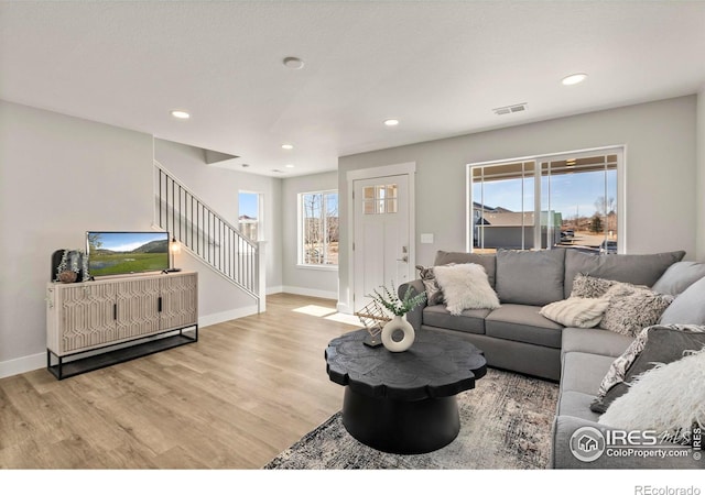 living room featuring light wood-style floors, plenty of natural light, stairway, and visible vents