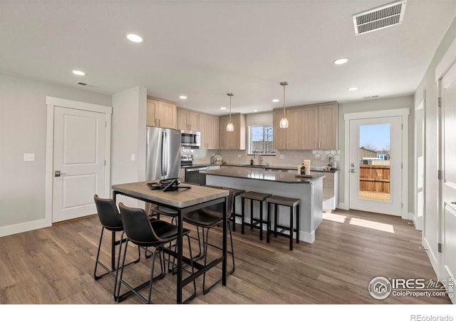 kitchen with visible vents, dark countertops, a kitchen island, appliances with stainless steel finishes, and pendant lighting