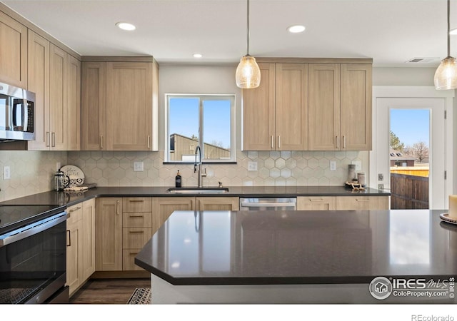 kitchen with light brown cabinets, a sink, appliances with stainless steel finishes, dark countertops, and decorative light fixtures