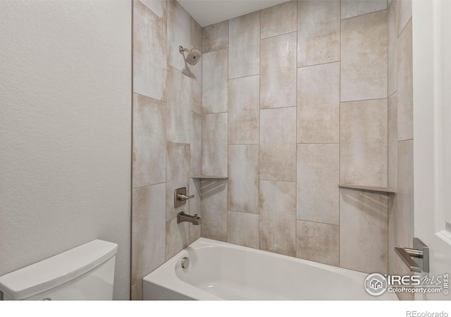 bathroom with toilet, a textured wall, and bathing tub / shower combination