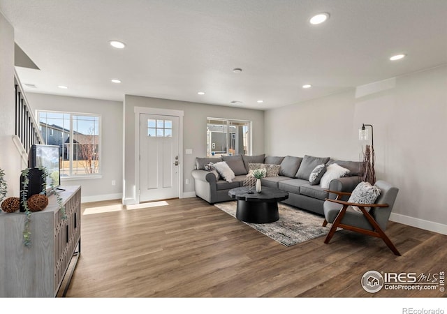 living room featuring baseboards, wood finished floors, stairs, and recessed lighting