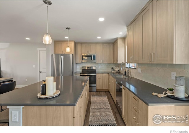 kitchen featuring dark countertops, a kitchen island, stainless steel appliances, light brown cabinetry, and a sink