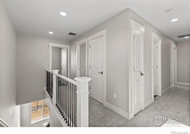 hallway with visible vents, baseboards, light colored carpet, an upstairs landing, and recessed lighting