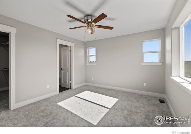 unfurnished bedroom featuring multiple windows, carpet flooring, a walk in closet, and visible vents