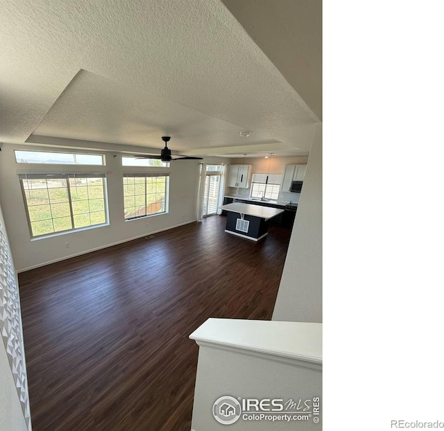3510 Valleywood Ct, Johnstown, CO 80534 - unfurnished living room featuring ceiling fan, dark wood-style flooring, a textured ceiling, and baseboards