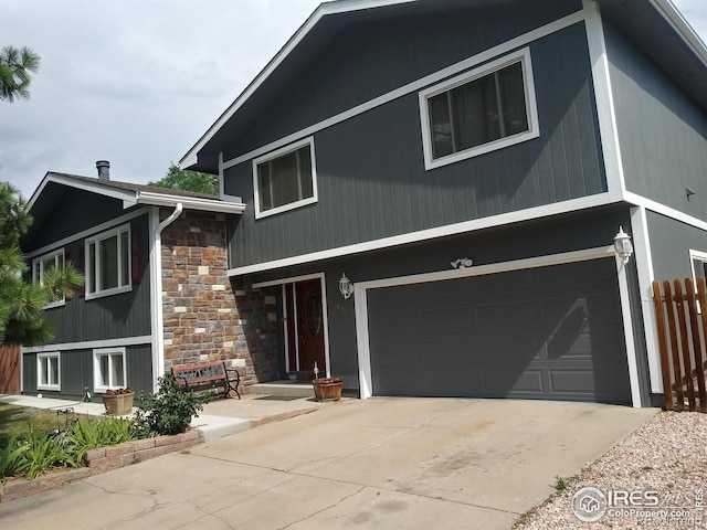 view of front of house featuring stone siding, driveway, an attached garage, and fence