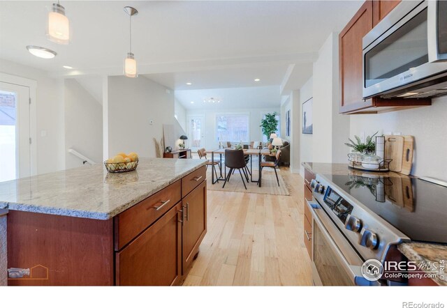 kitchen featuring open floor plan, hanging light fixtures, appliances with stainless steel finishes, light wood-type flooring, and a center island