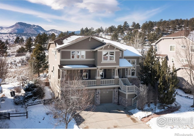 view of front of property with an attached garage, a mountain view, fence, stone siding, and driveway