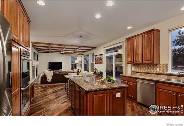 kitchen with dark wood finished floors, a kitchen island, appliances with stainless steel finishes, open floor plan, and a sink