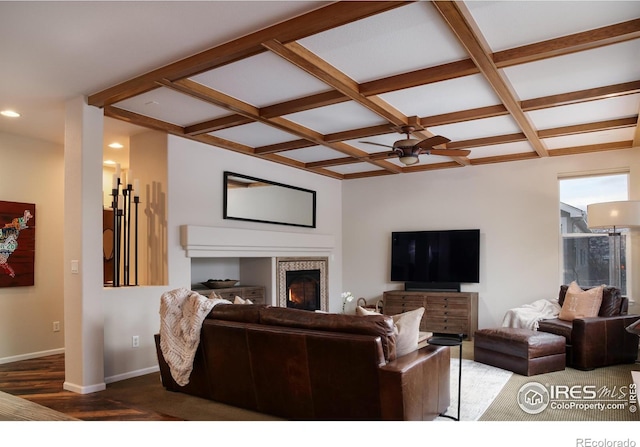 living room featuring a warm lit fireplace, baseboards, coffered ceiling, and a ceiling fan