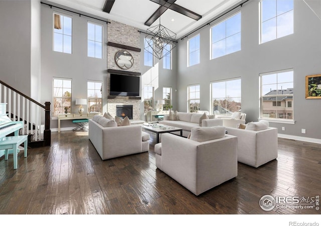 living room with a healthy amount of sunlight, a notable chandelier, dark hardwood / wood-style floors, and a stone fireplace