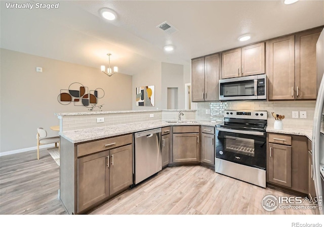 kitchen with appliances with stainless steel finishes, sink, kitchen peninsula, light stone countertops, and decorative backsplash