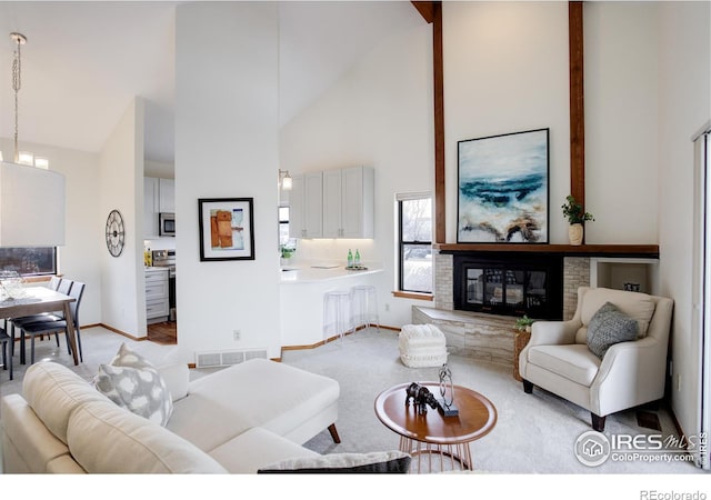 living area with high vaulted ceiling, light carpet, visible vents, baseboards, and a glass covered fireplace