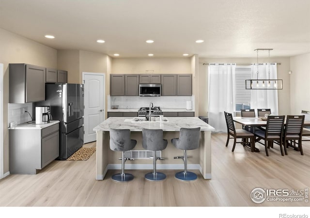 kitchen with appliances with stainless steel finishes, an island with sink, gray cabinets, and light stone countertops