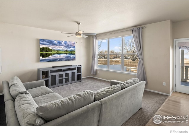 living area featuring light wood-type flooring, a textured ceiling, baseboards, and a ceiling fan