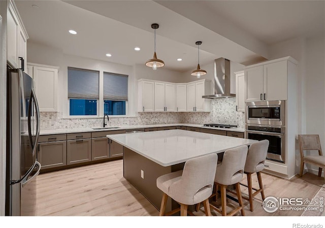 kitchen with sink, a kitchen island, decorative light fixtures, stainless steel appliances, and wall chimney exhaust hood