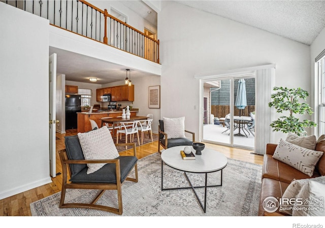 living area featuring a textured ceiling, high vaulted ceiling, light wood-type flooring, and baseboards