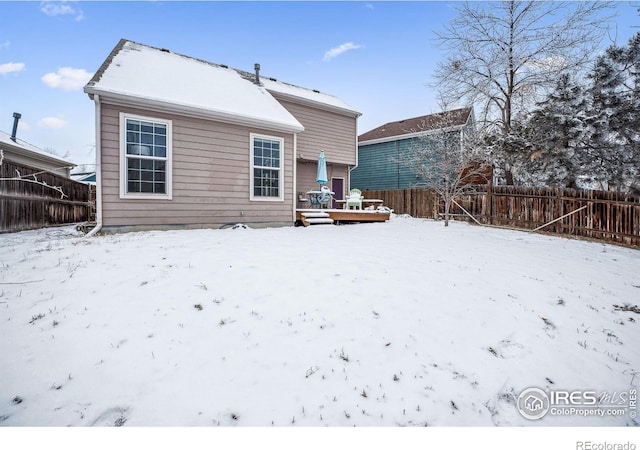 snow covered back of property featuring fence and a deck