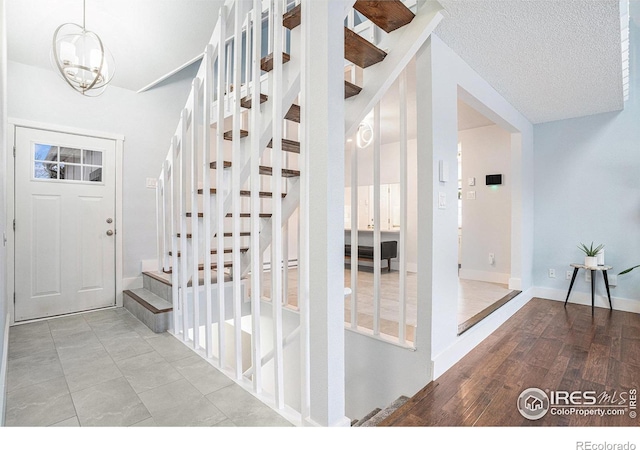 entryway featuring stairs, baseboards, a chandelier, a textured ceiling, and light wood finished floors