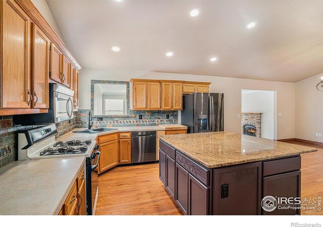 kitchen featuring a sink, light stone counters, brown cabinets, stainless steel appliances, and light wood-type flooring