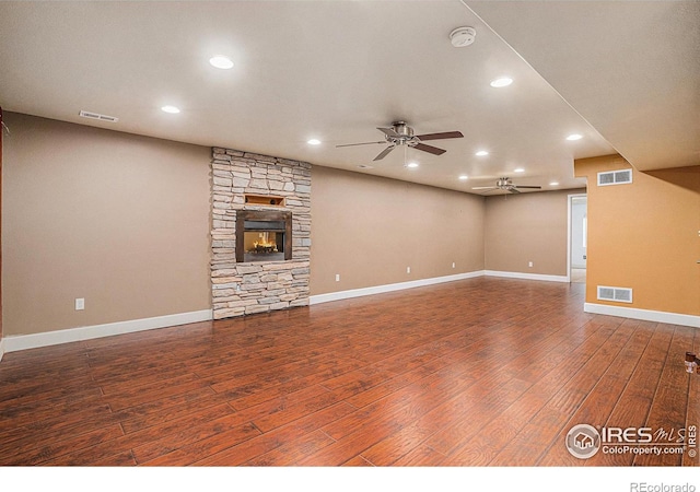 unfurnished living room featuring visible vents, dark wood-style flooring, and a stone fireplace