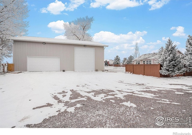 snow covered garage with a garage and fence