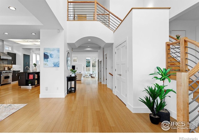 foyer with baseboards, light wood finished floors, arched walkways, stairs, and recessed lighting