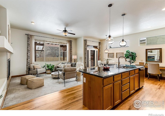 kitchen featuring brown cabinets, a sink, a kitchen island with sink, ceiling fan, and light wood-style floors