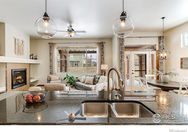 kitchen with a tile fireplace, decorative light fixtures, dark stone counters, and a sink