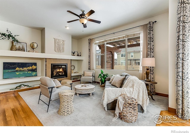 living room featuring a ceiling fan, a tile fireplace, baseboards, and wood finished floors