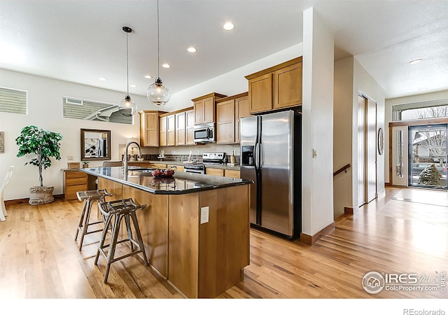 kitchen featuring a breakfast bar area, dark countertops, a center island with sink, light wood-type flooring, and appliances with stainless steel finishes