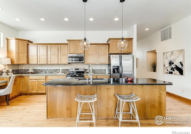 kitchen with a sink, stainless steel appliances, light wood-type flooring, visible vents, and decorative backsplash