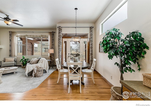 dining area with baseboards, light wood-style flooring, and ceiling fan with notable chandelier