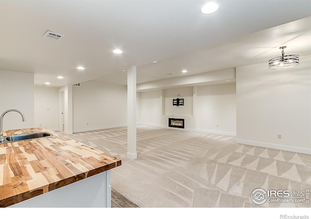finished below grade area with a sink, light colored carpet, visible vents, recessed lighting, and a glass covered fireplace
