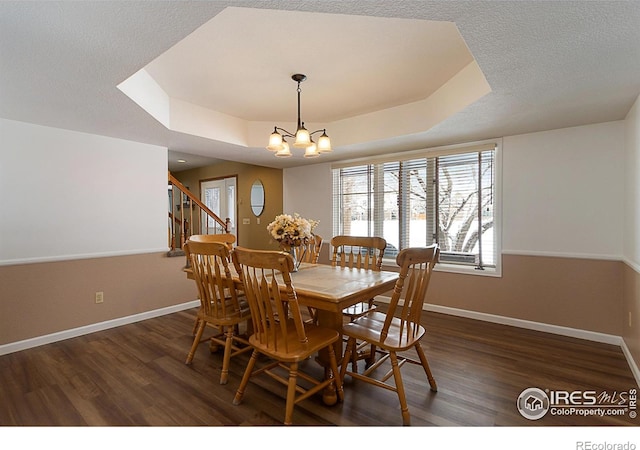 dining area with a chandelier, a raised ceiling, dark wood finished floors, and baseboards