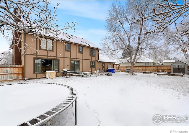 snow covered back of property with an outdoor structure, fence, a storage shed, and stucco siding