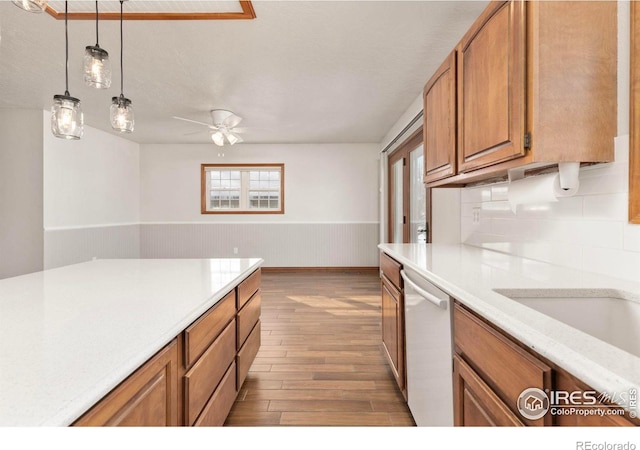 kitchen with brown cabinetry, dishwasher, light wood-style flooring, decorative light fixtures, and light countertops