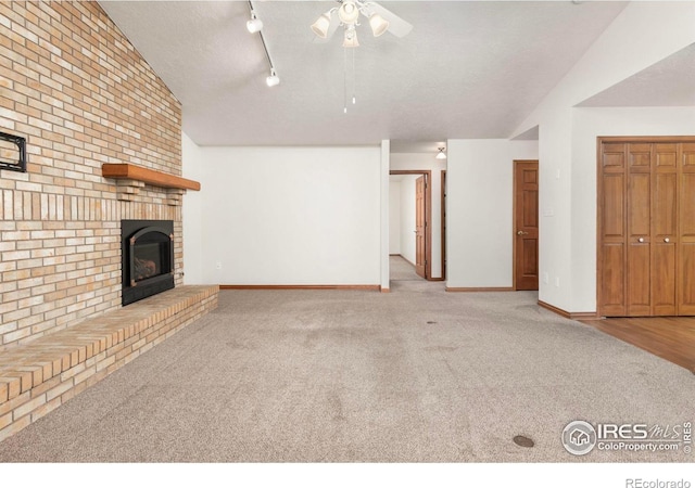 unfurnished living room with baseboards, light colored carpet, vaulted ceiling, a textured ceiling, and a fireplace