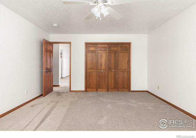 unfurnished bedroom featuring light carpet, a textured ceiling, a closet, and baseboards