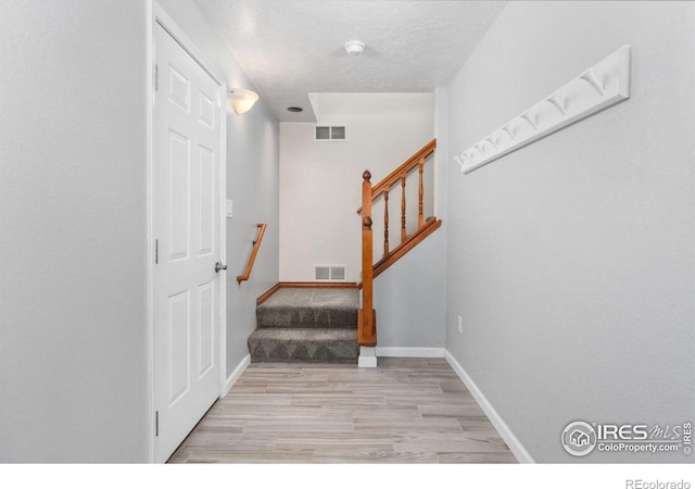 stairs featuring baseboards, a textured ceiling, visible vents, and wood finished floors