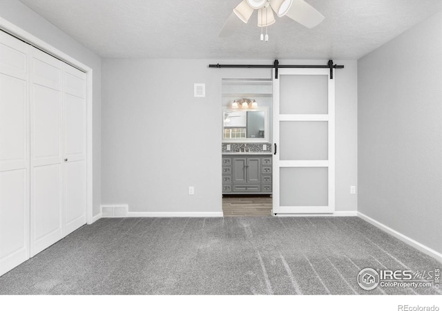 unfurnished bedroom with a barn door, baseboards, visible vents, a textured ceiling, and carpet flooring