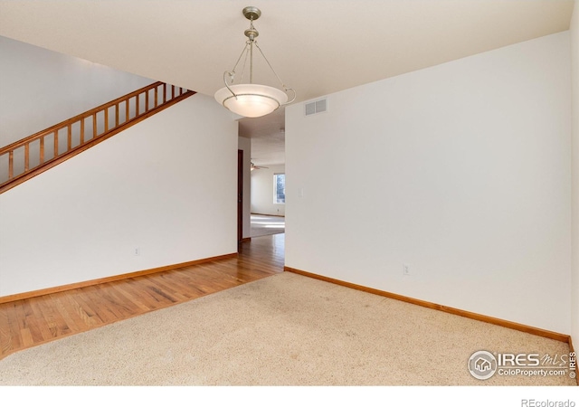 carpeted empty room with visible vents, stairway, baseboards, and wood finished floors