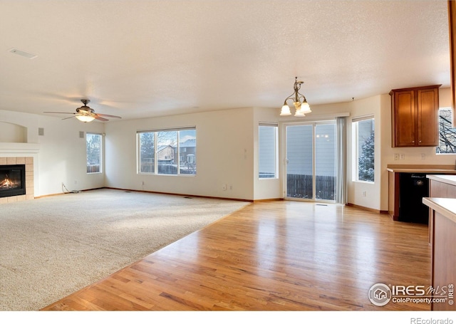 unfurnished living room featuring a fireplace, a textured ceiling, light wood-type flooring, baseboards, and ceiling fan with notable chandelier