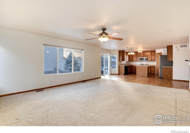 unfurnished living room featuring light carpet, ceiling fan, visible vents, and baseboards