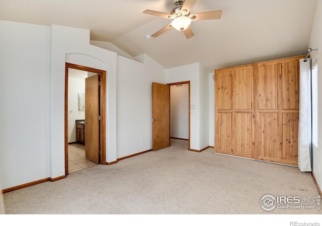 unfurnished bedroom featuring light carpet, baseboards, vaulted ceiling, and ensuite bathroom