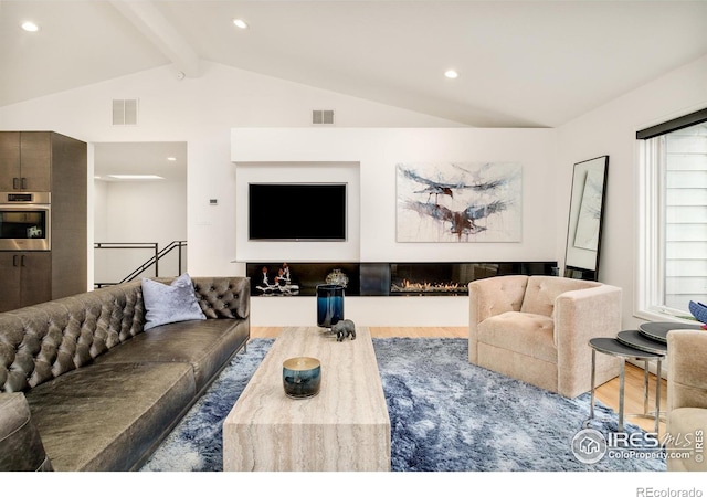 living room featuring lofted ceiling with beams, visible vents, wood finished floors, and a glass covered fireplace