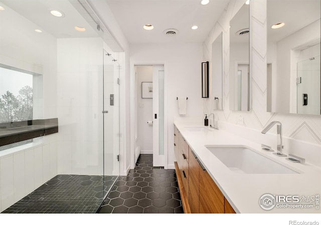 full bathroom featuring a tile shower, double vanity, a sink, and visible vents