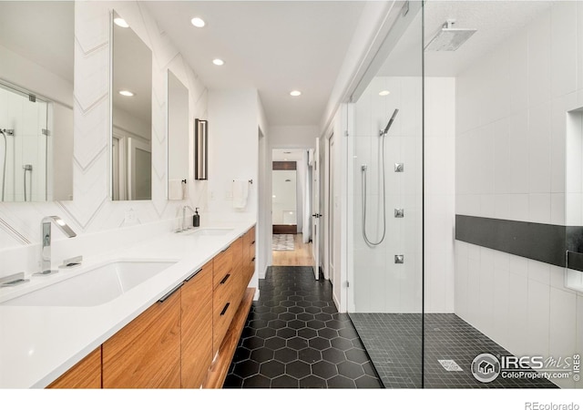 bathroom with double vanity, tiled shower, a sink, and tile patterned floors