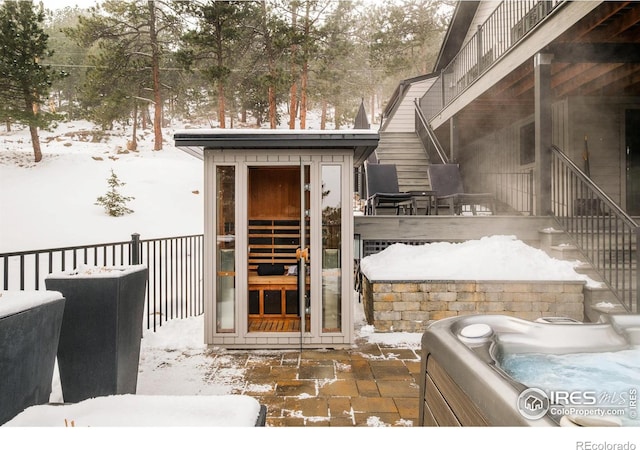 snow covered property entrance with fence and a hot tub